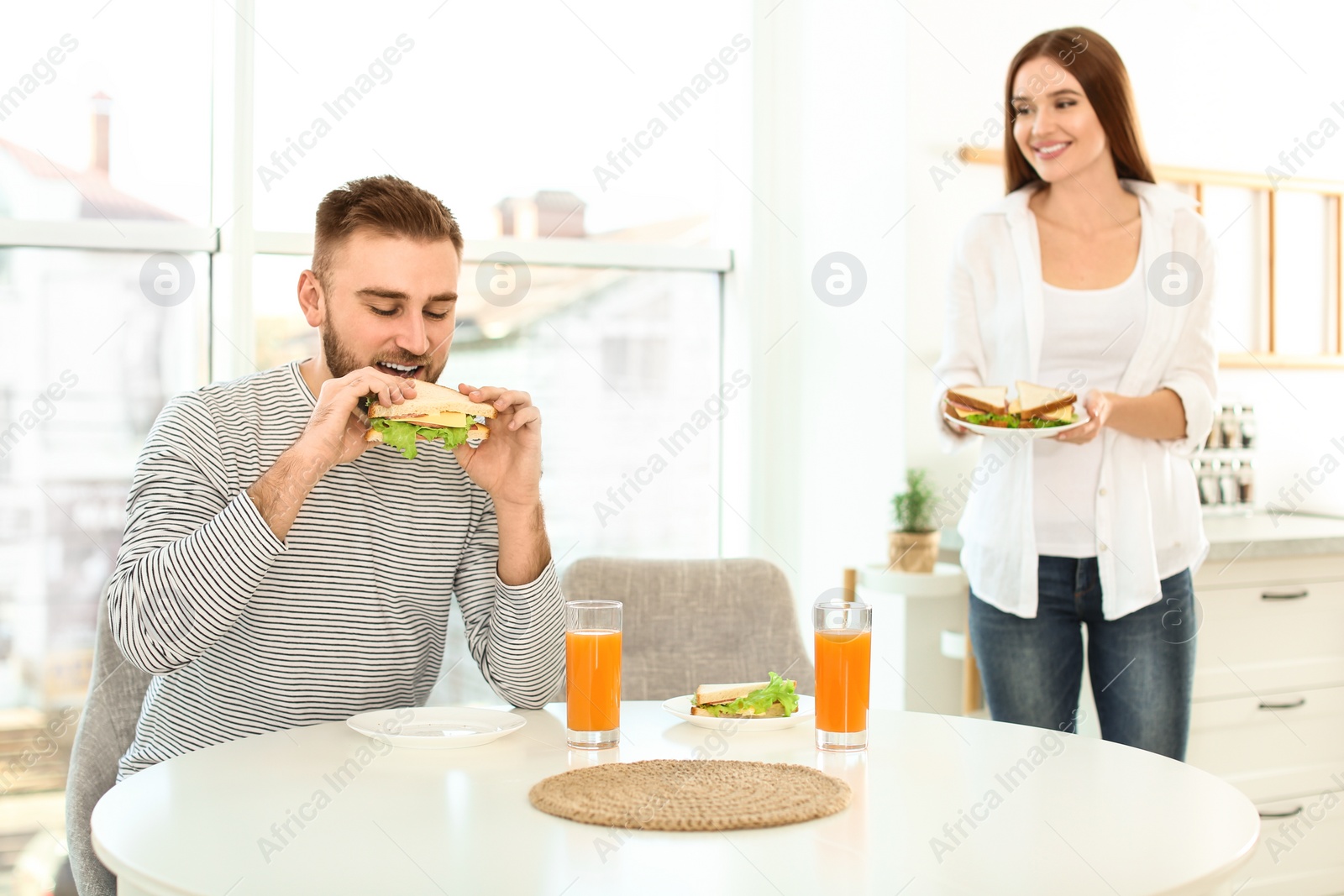 Photo of Happy couple having breakfast with sandwiches at table in kitchen