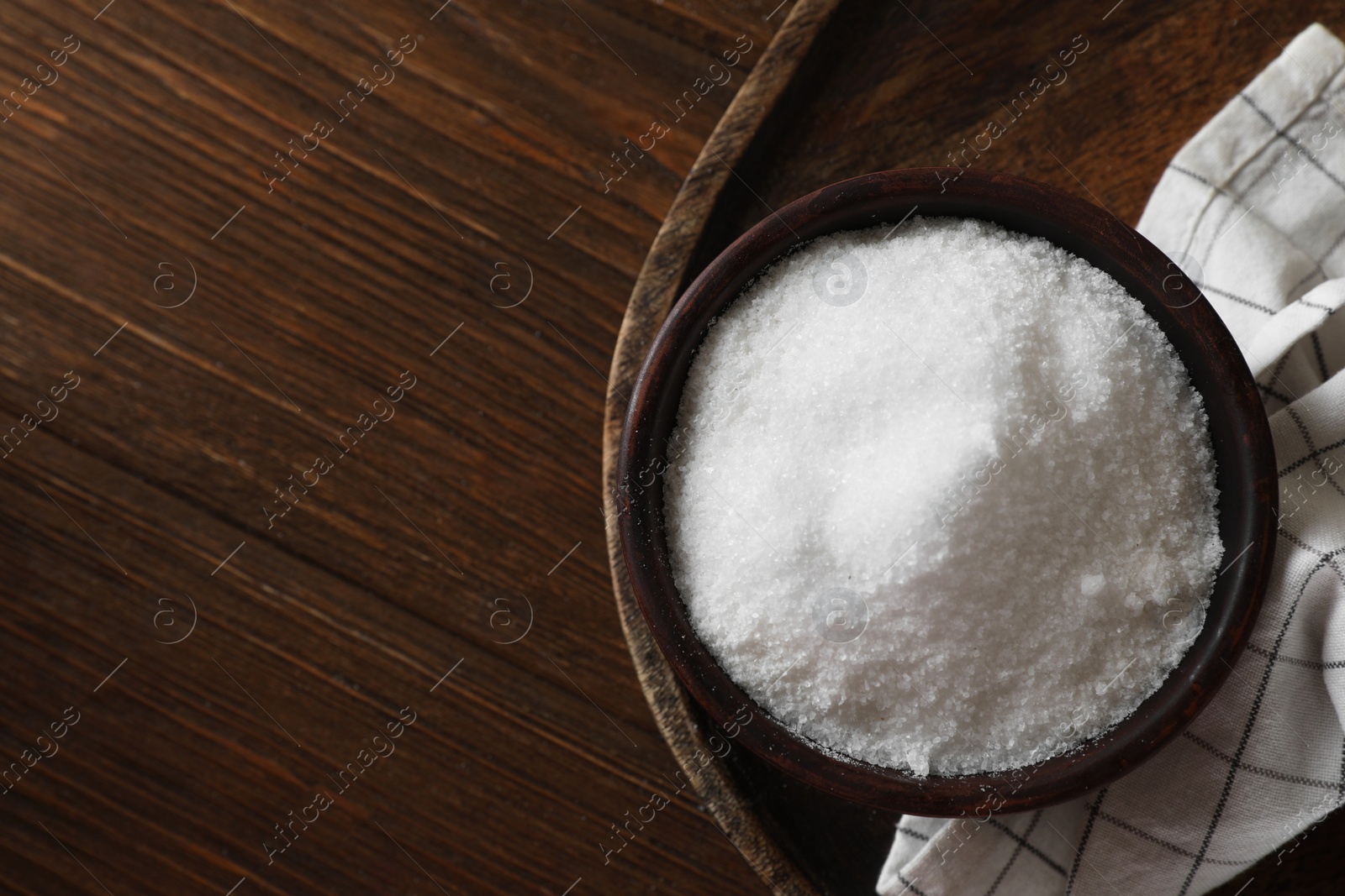 Photo of Organic salt in bowl on wooden table, top view. Space for text