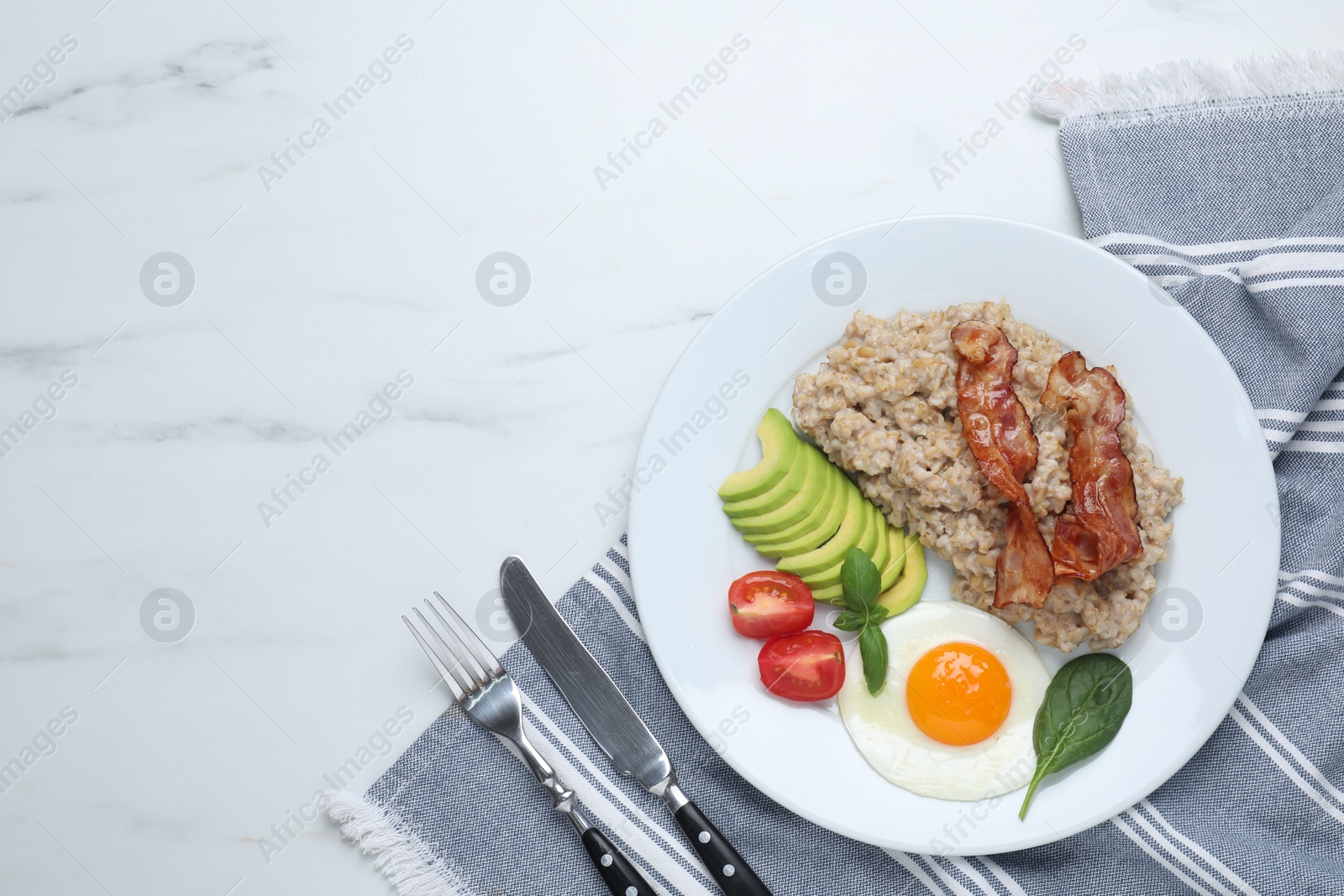 Photo of Delicious boiled oatmeal with fried egg, bacon, avocado and tomato served on white marble table, flat lay. Space for text