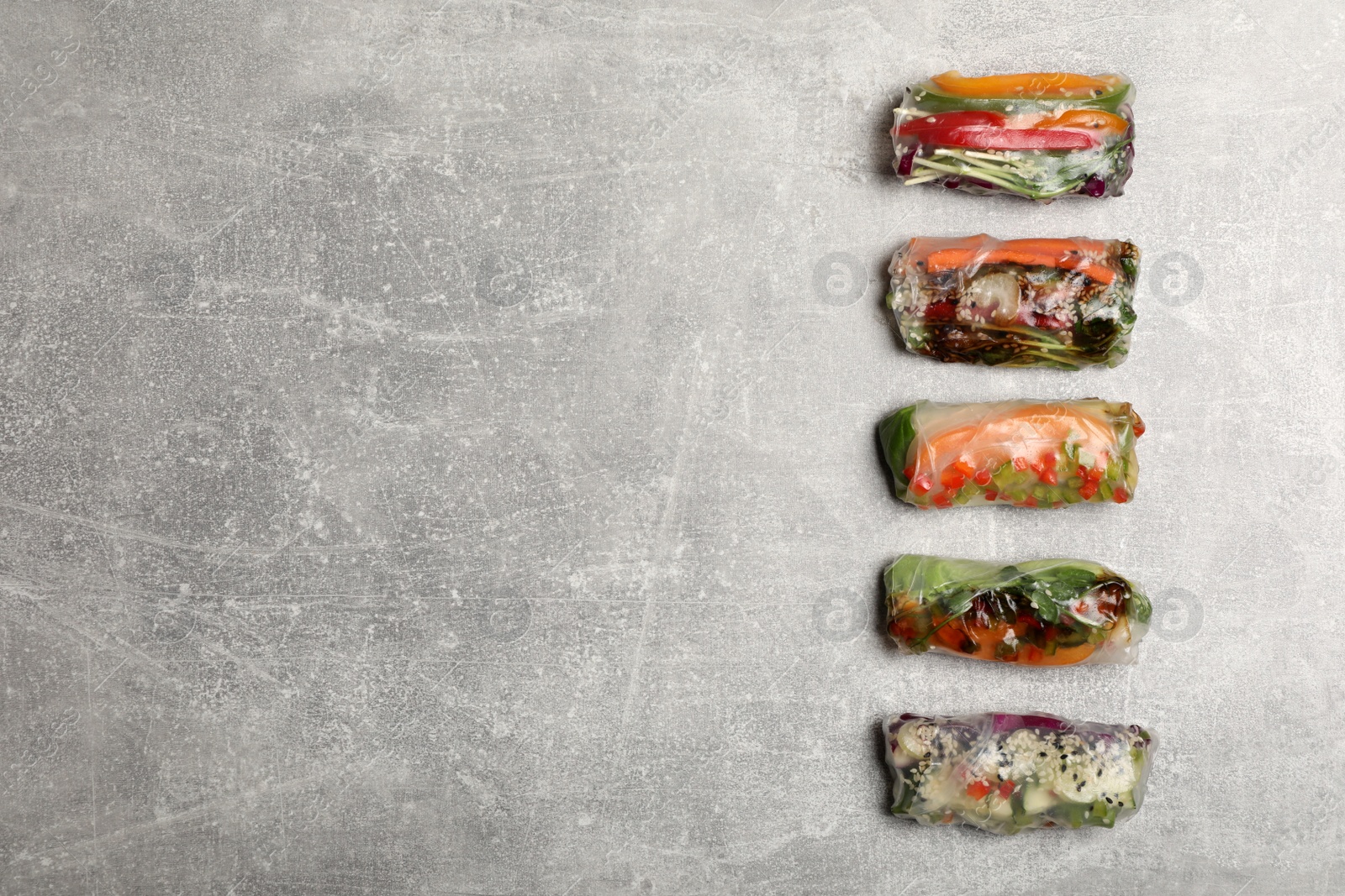 Photo of Many different delicious rolls wrapped in rice paper on grey table, flat lay. Space for text