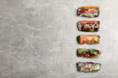 Many different delicious rolls wrapped in rice paper on grey table, flat lay. Space for text