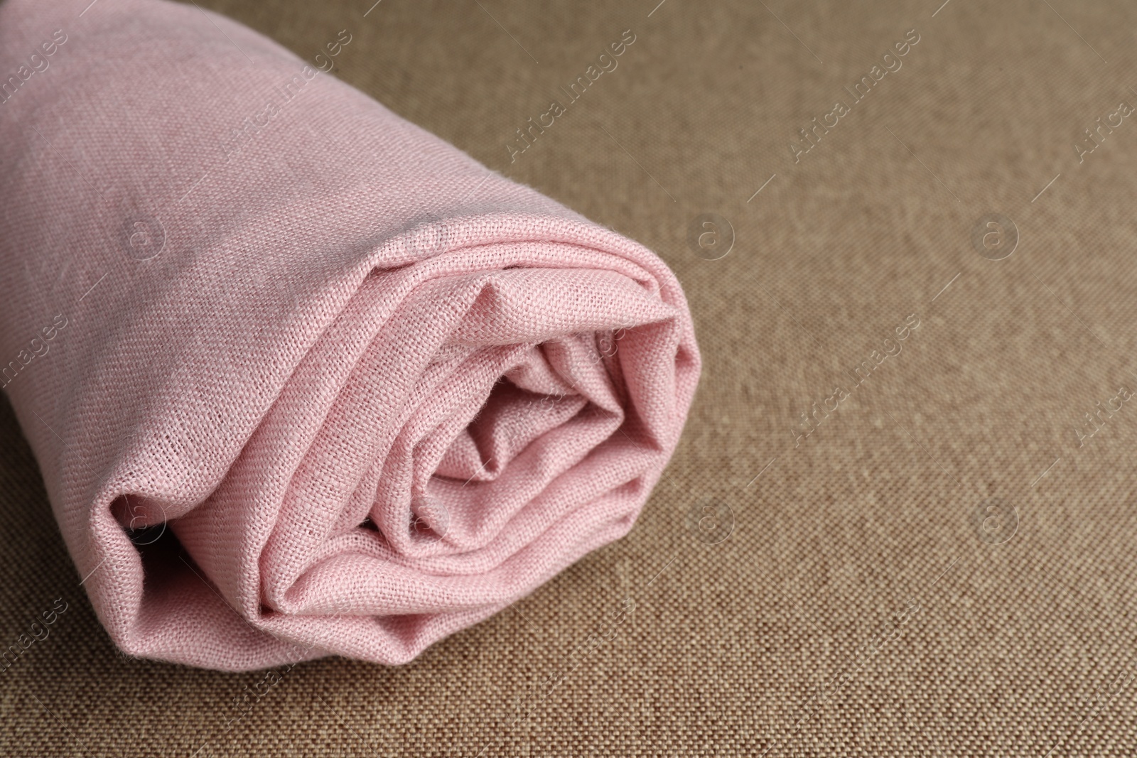 Photo of Rolled pink fabric on brown cloth, closeup. Space for text
