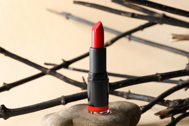 Beautiful red lipstick on stone and tree twigs against beige background