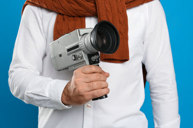 Man with vintage video camera on light blue background, closeup