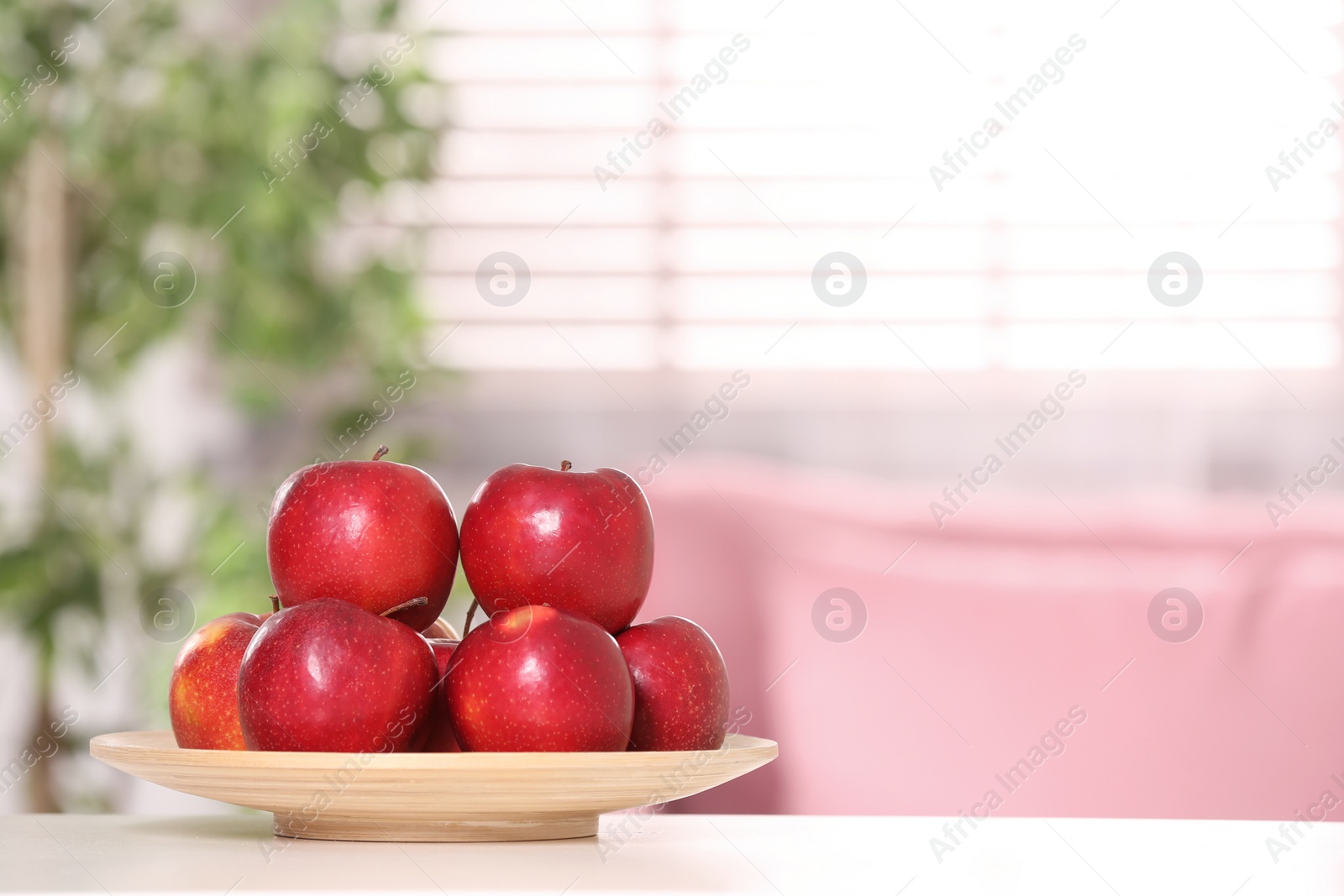 Photo of Plate with sweet red apples on table in room, space for text