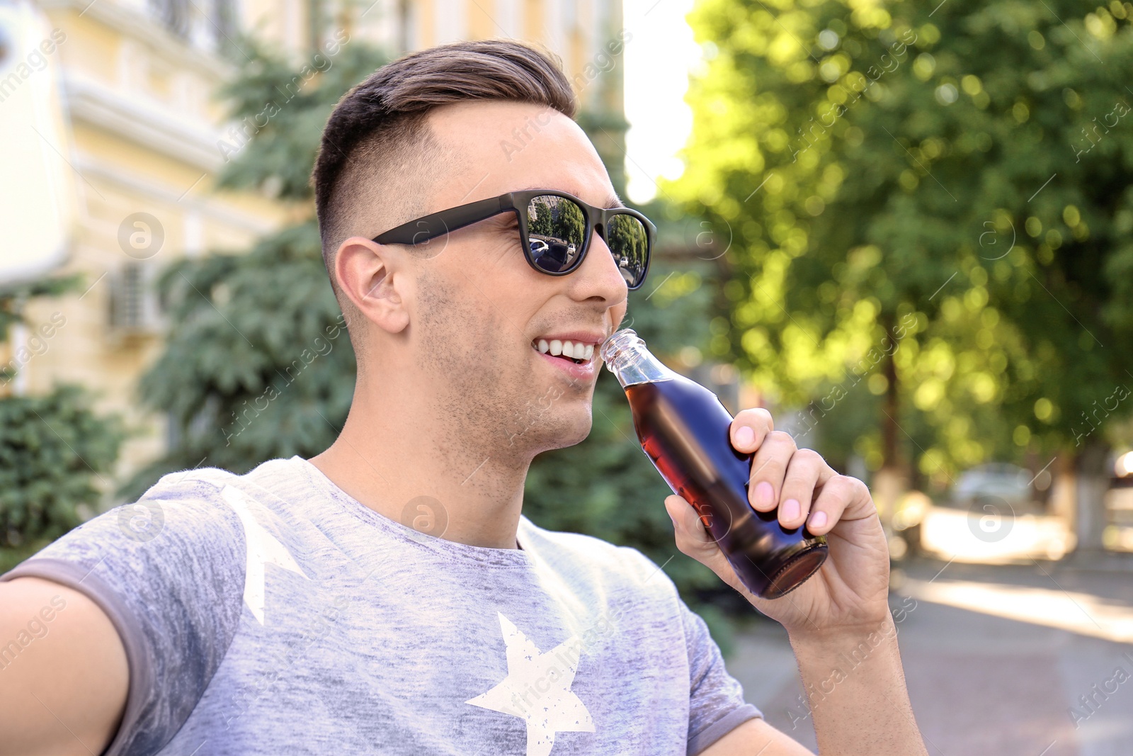 Photo of Young man with bottle of cola taking selfie outdoors