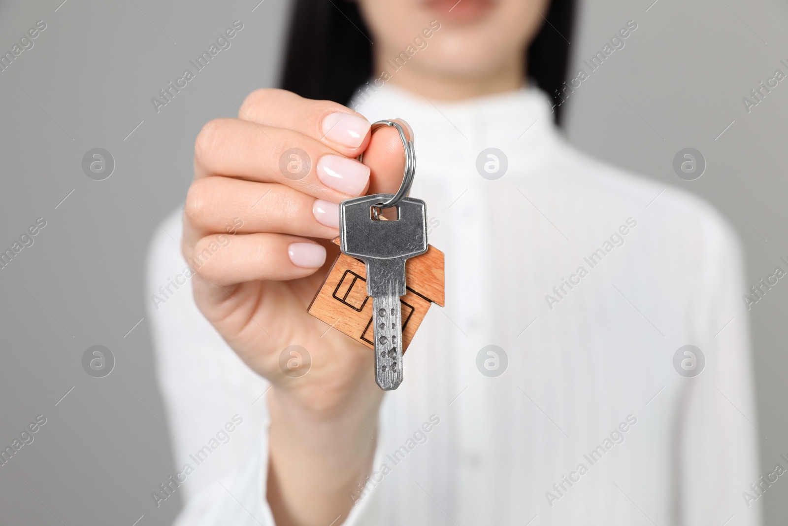 Photo of Real estate agent holding key against grey background, closeup