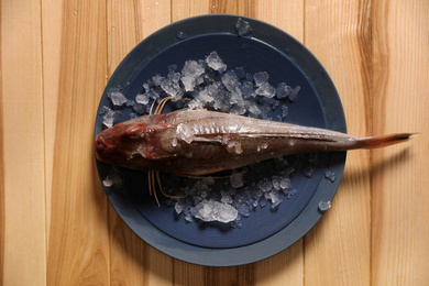 Photo of Fresh raw fish with ice on wooden table, top view