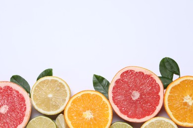 Different cut citrus fruits and leaves on white table, flat lay. Space for text