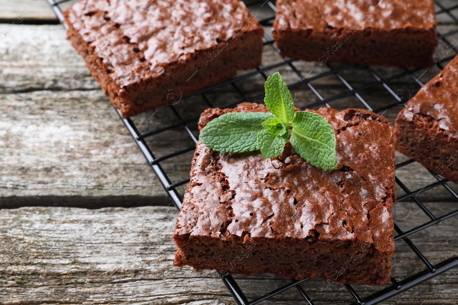 Photo of Cooling rack with delicious chocolate brownies and fresh mint on wooden table, closeup