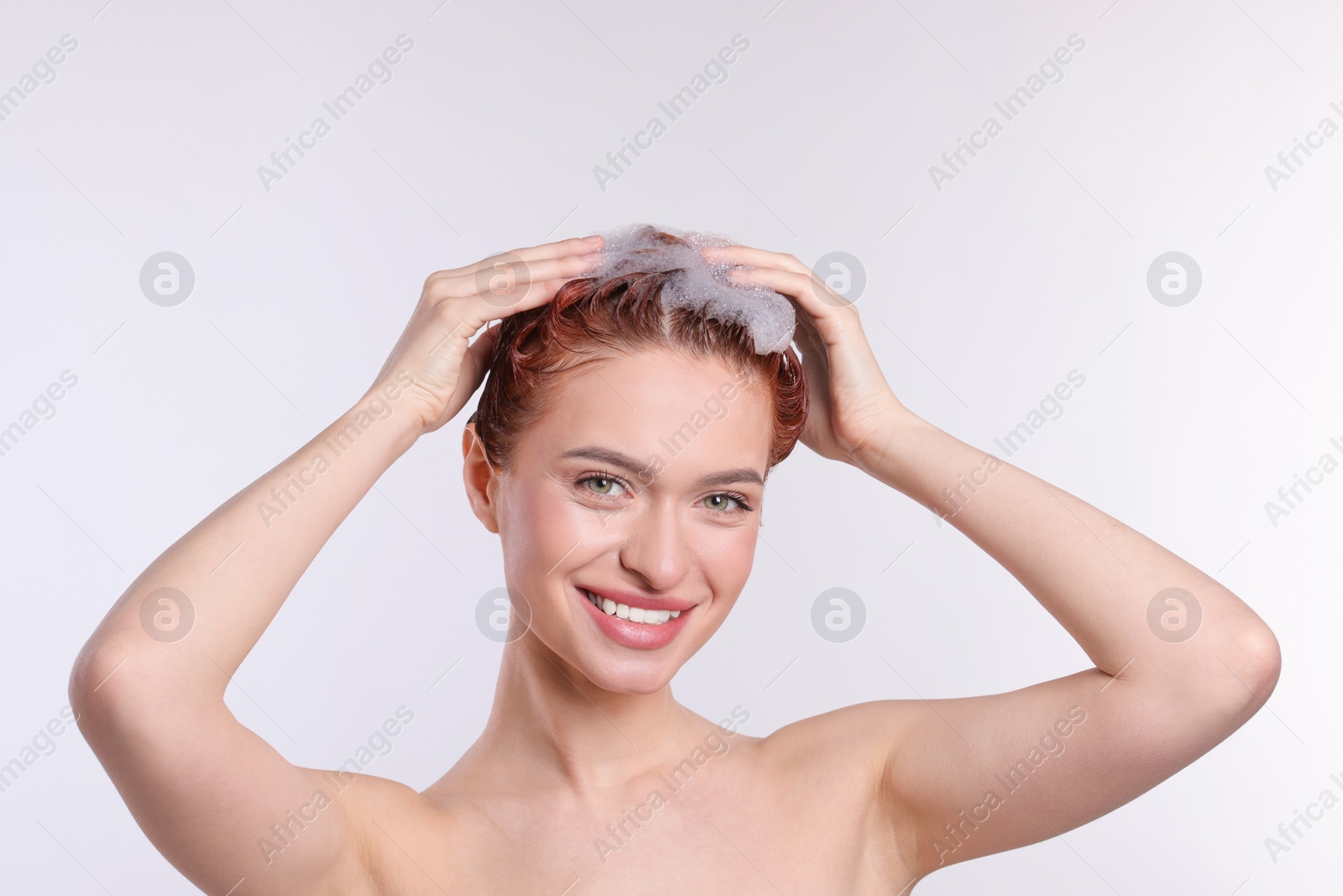 Photo of Happy young woman washing her hair with shampoo on light grey background