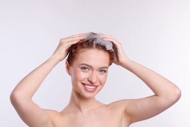 Happy young woman washing her hair with shampoo on light grey background