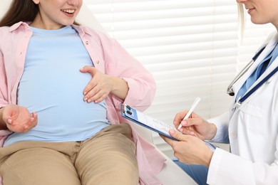 Photo of Doctor with results of laboratory test consulting smiling pregnant patient in clinic, closeup