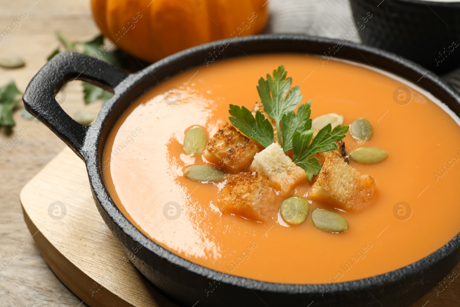 Photo of Tasty creamy pumpkin soup with croutons, seeds and parsley in bowl on table, closeup