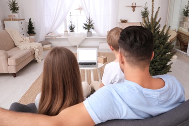 Photo of Family with child using video chat on laptop in room decorated for Christmas, back view