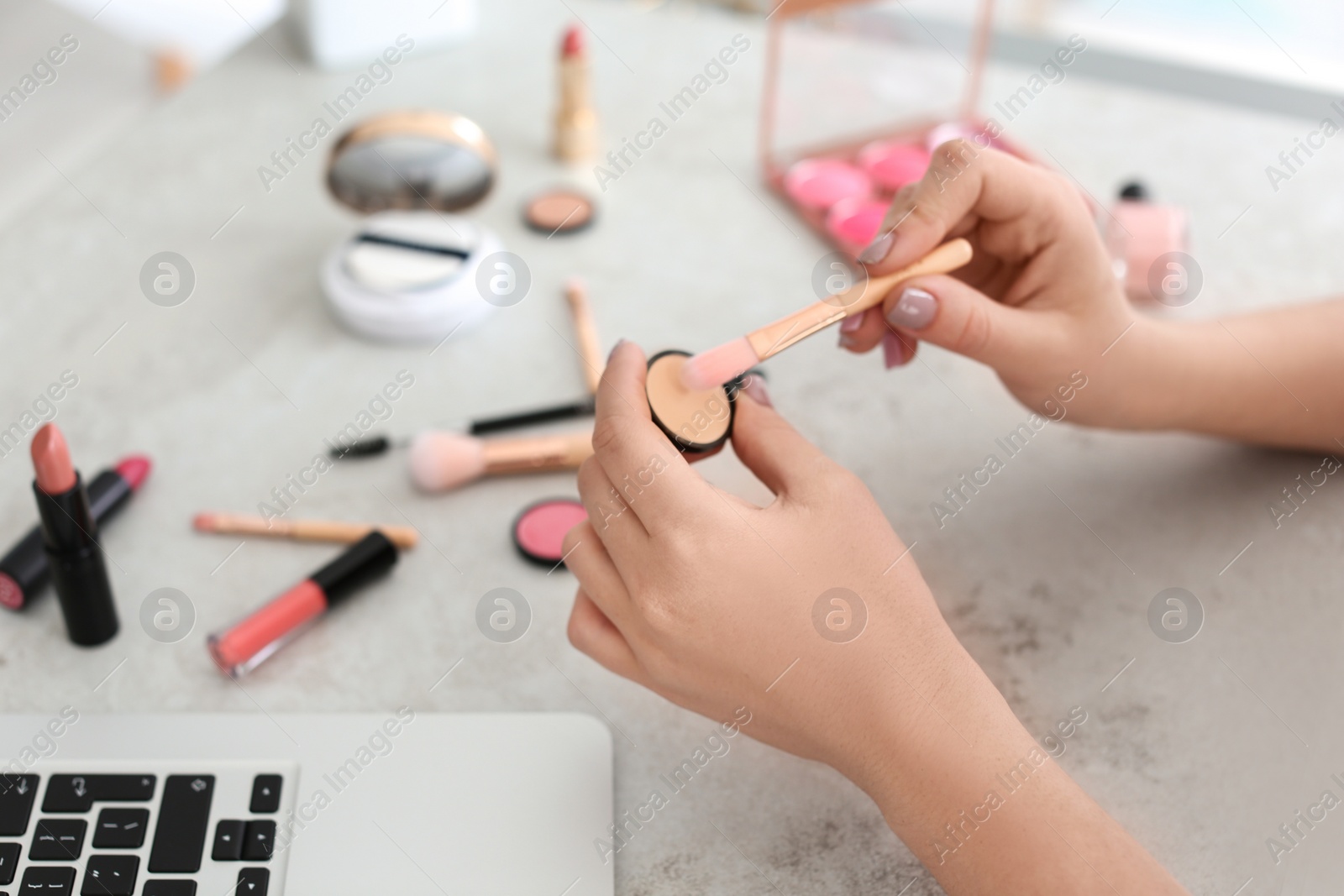 Photo of Young woman with makeup products and laptop at table. Beauty blogger