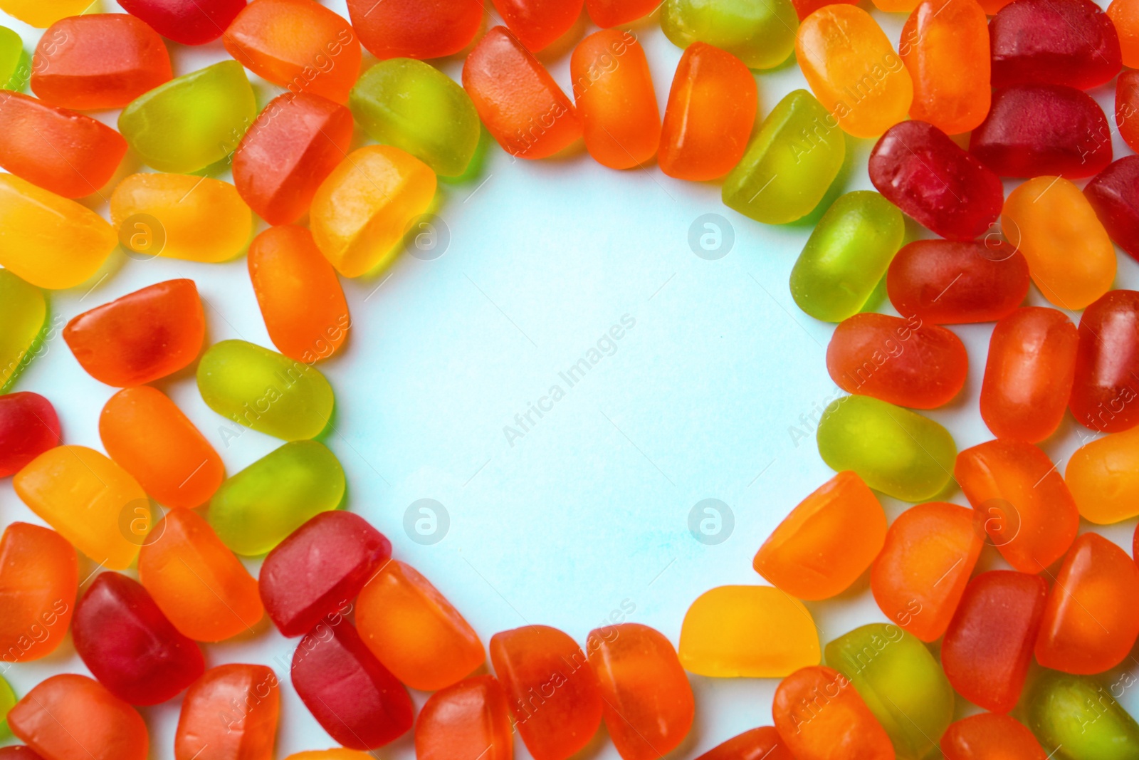 Photo of Frame of sweet jelly candies on blue background, top view. Space for text