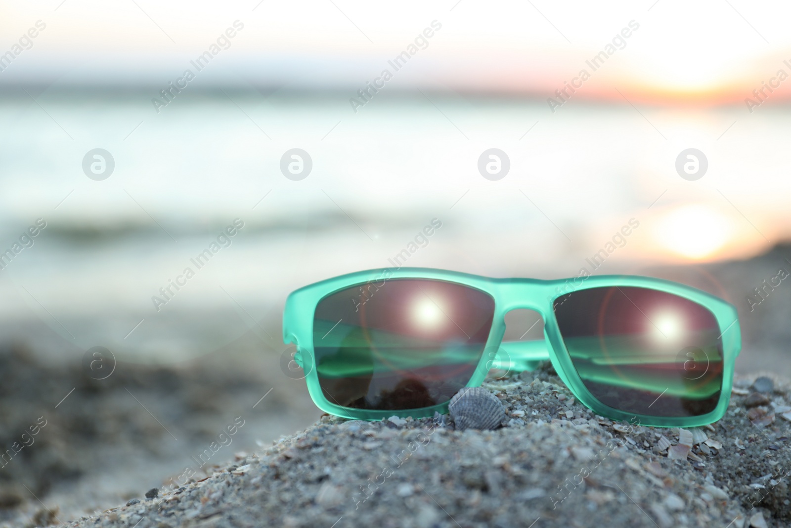 Photo of Stylish sunglasses on sandy beach at sunset