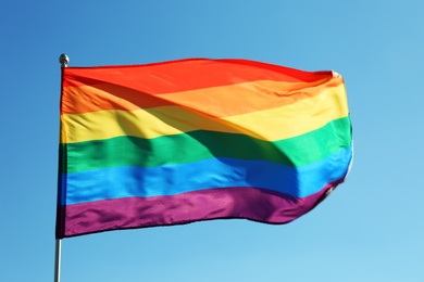 Photo of Rainbow LGBT flag fluttering on blue sky background. Gay rights movement