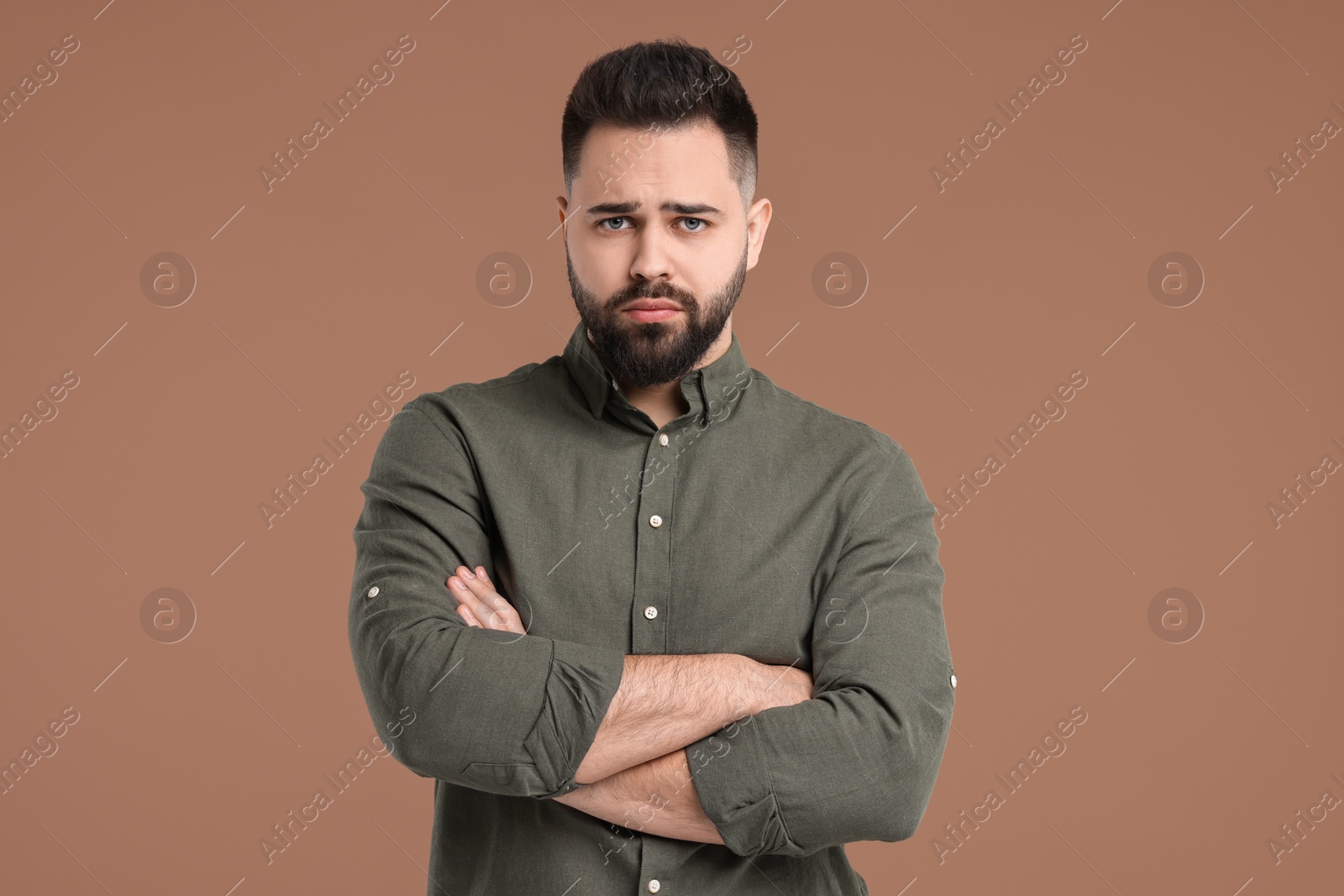 Photo of Portrait of sad man with crossed arms on brown background