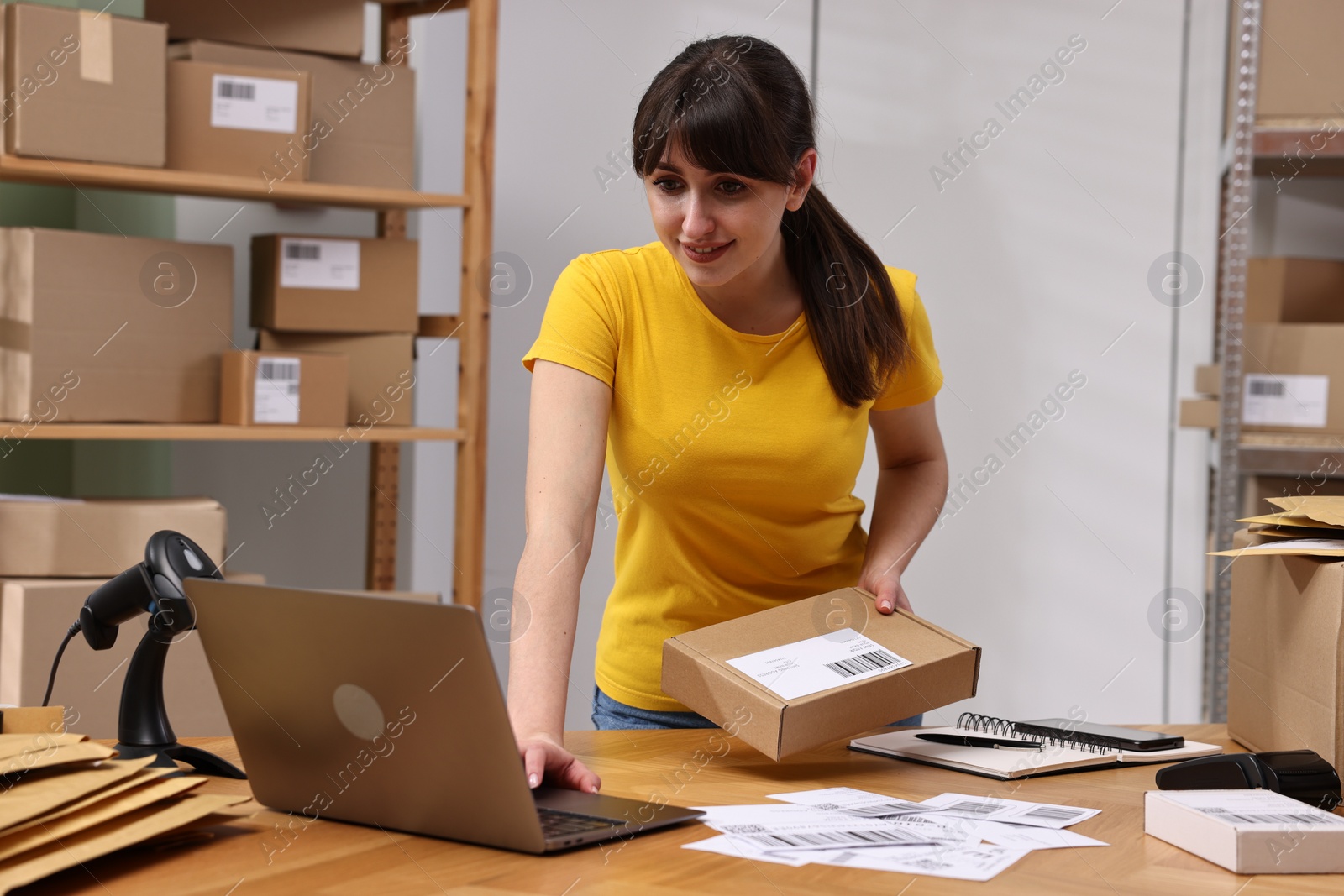 Photo of Parcel packing. Post office worker with box using laptop at wooden table indoors