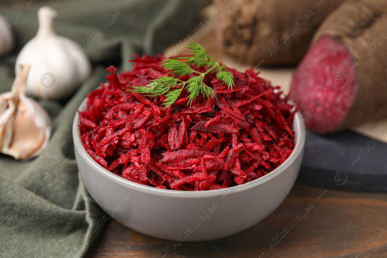 Photo of Grated red beet and dill in bowl on table, closeup