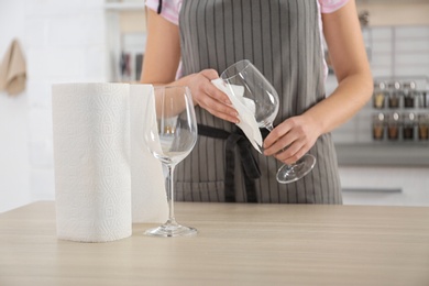 Woman wiping wine glass with paper towel in kitchen, closeup