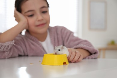 Photo of Little girl with cute hamster at table indoors, focus on hand