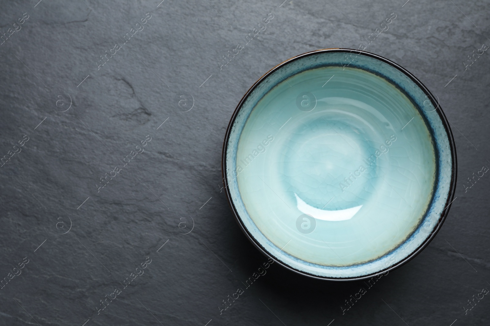 Photo of Clean bowl on black slate table, top view. Space for text