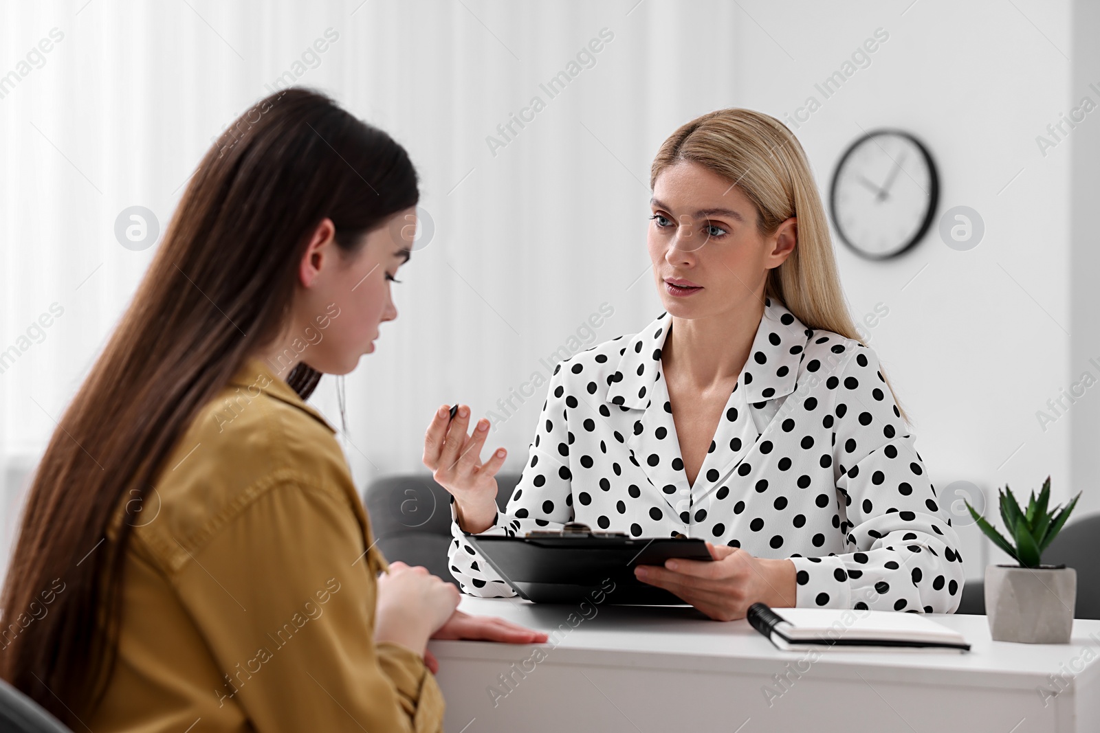 Photo of Psychologist holding clipboard while working with teenage girl at table in office