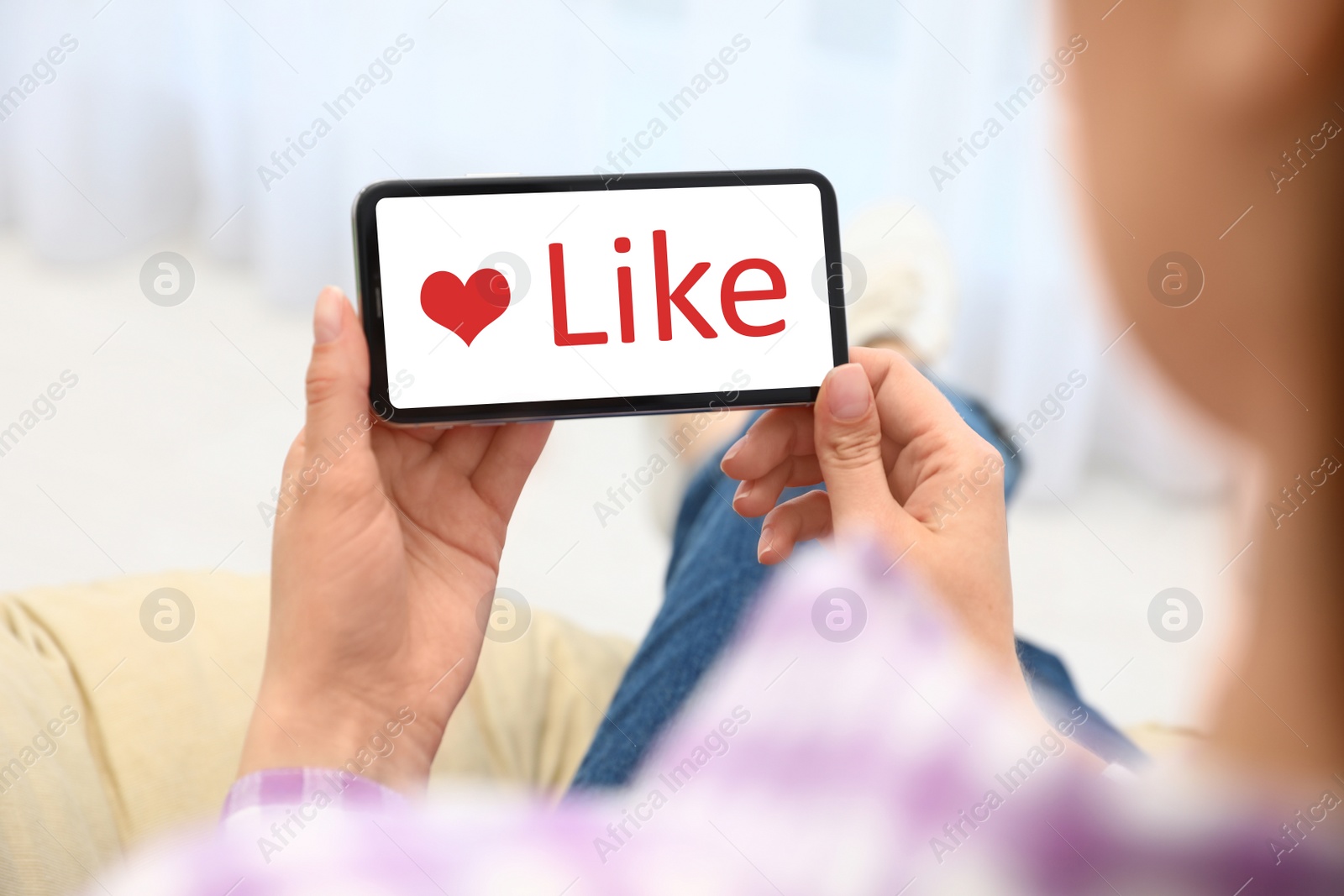 Image of Woman holding smartphone with word Like on screen indoors, closeup