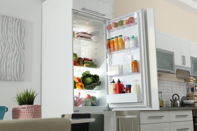 Photo of Open refrigerator full of products in stylish kitchen interior