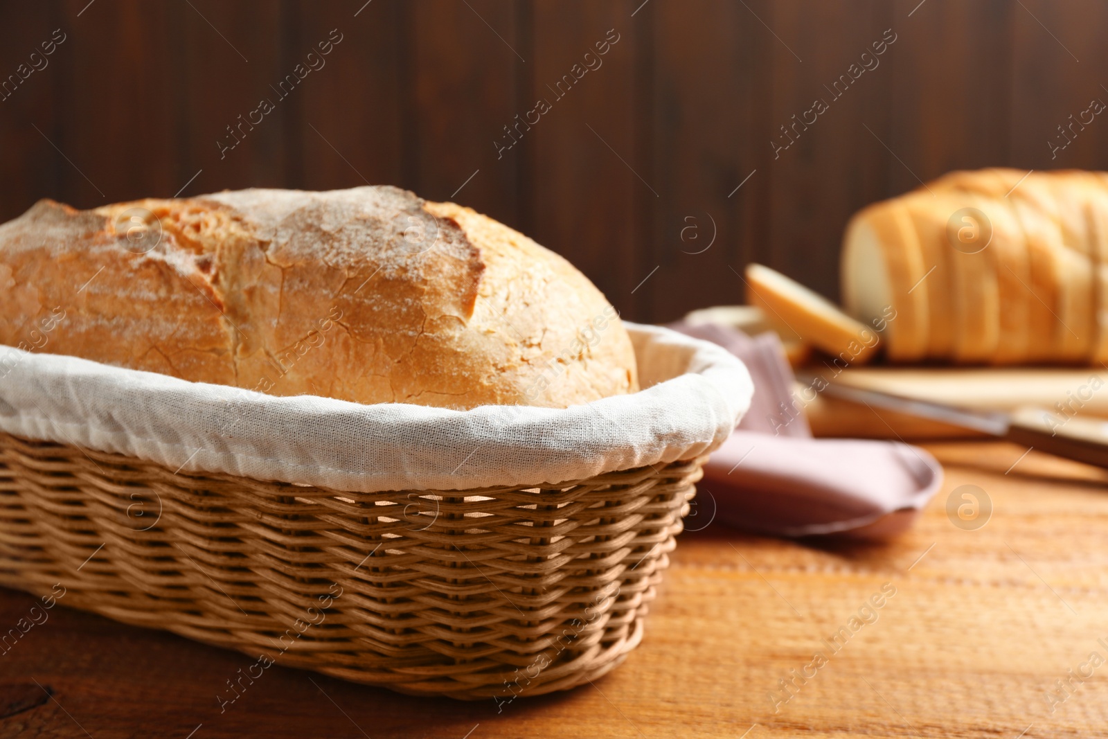 Photo of Loaf of tasty fresh bread in wicker basket on wooden table