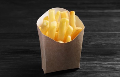 Delicious french fries in paper box on black wooden table, closeup