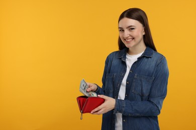 Happy woman putting money into wallet on orange background, space for text