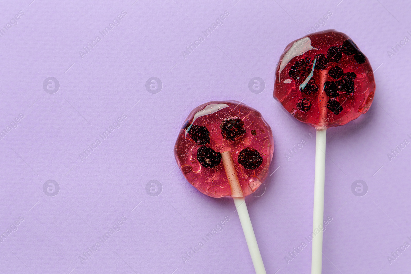 Photo of Sweet colorful lollipops with berries on lilac background, flat lay. Space for text