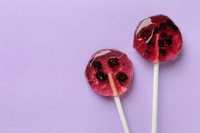 Photo of Sweet colorful lollipops with berries on lilac background, flat lay. Space for text