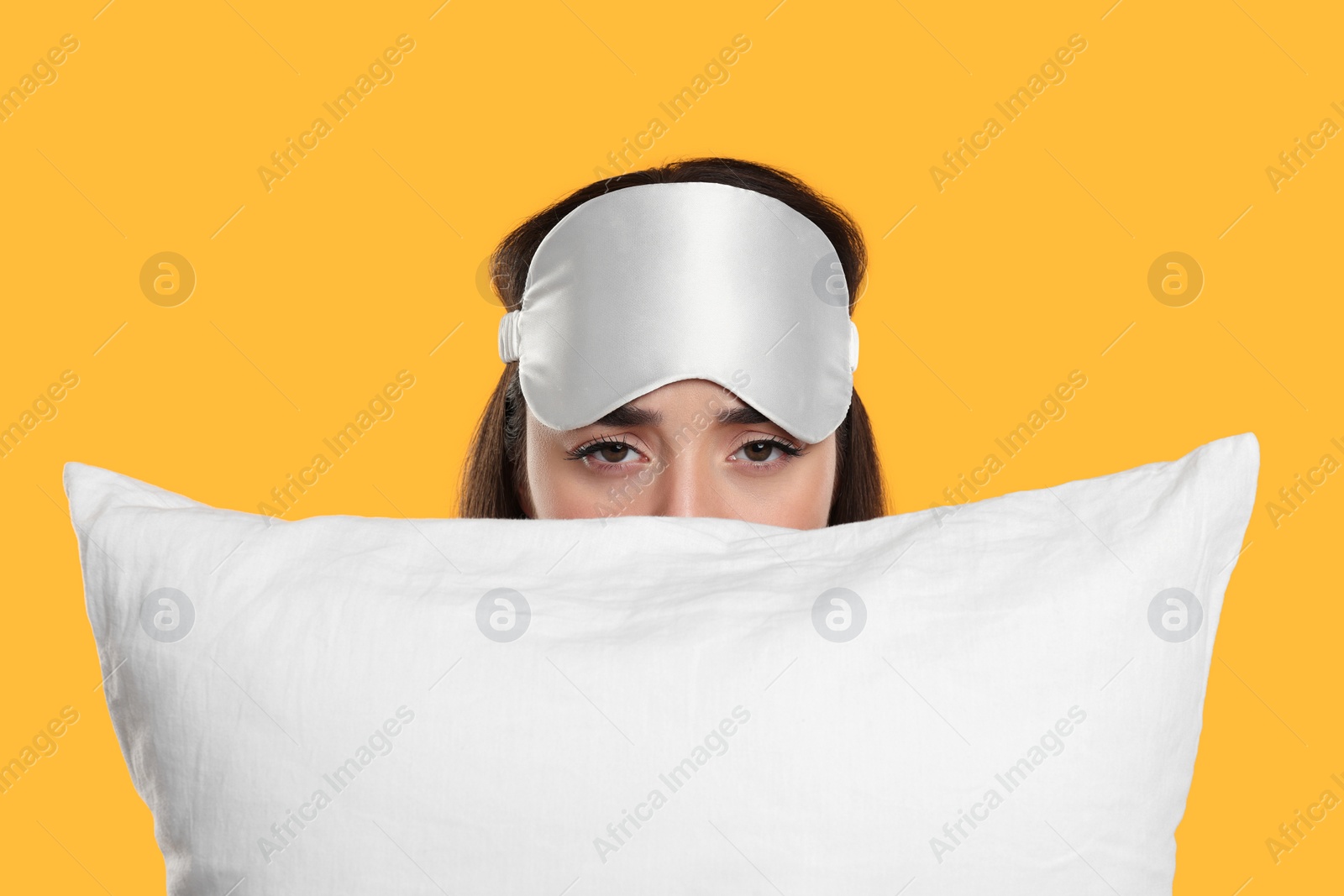 Photo of Tired young woman with sleep mask and pillow on yellow background. Insomnia problem