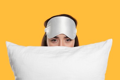Tired young woman with sleep mask and pillow on yellow background. Insomnia problem