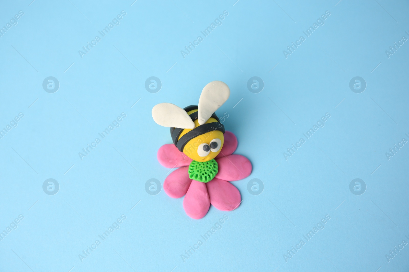Photo of Bee with flower made from plasticine on light blue background. Children's handmade ideas