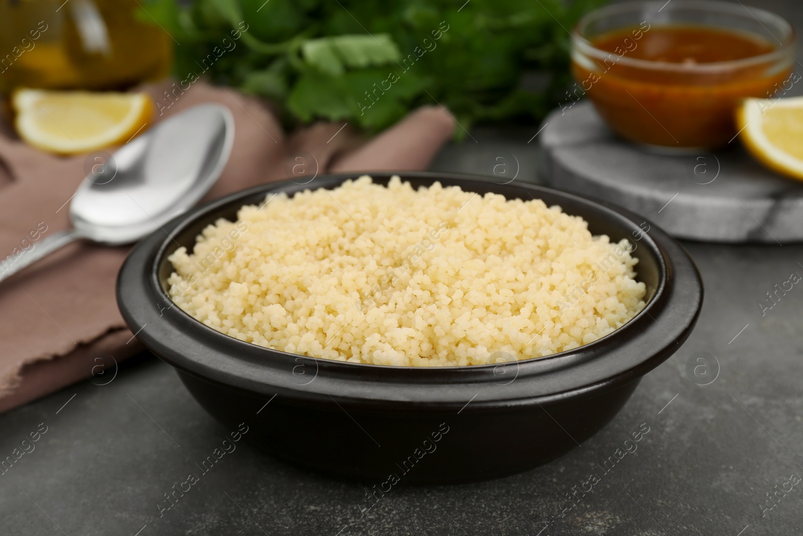 Photo of Bowl of tasty couscous on grey table, closeup