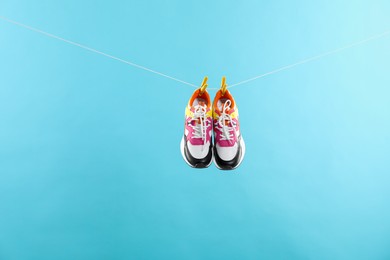 Photo of Stylish sneakers drying on washing line against light blue background