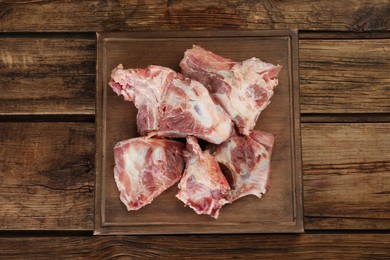 Photo of Cutting board with raw chopped meaty bones on wooden table, top view