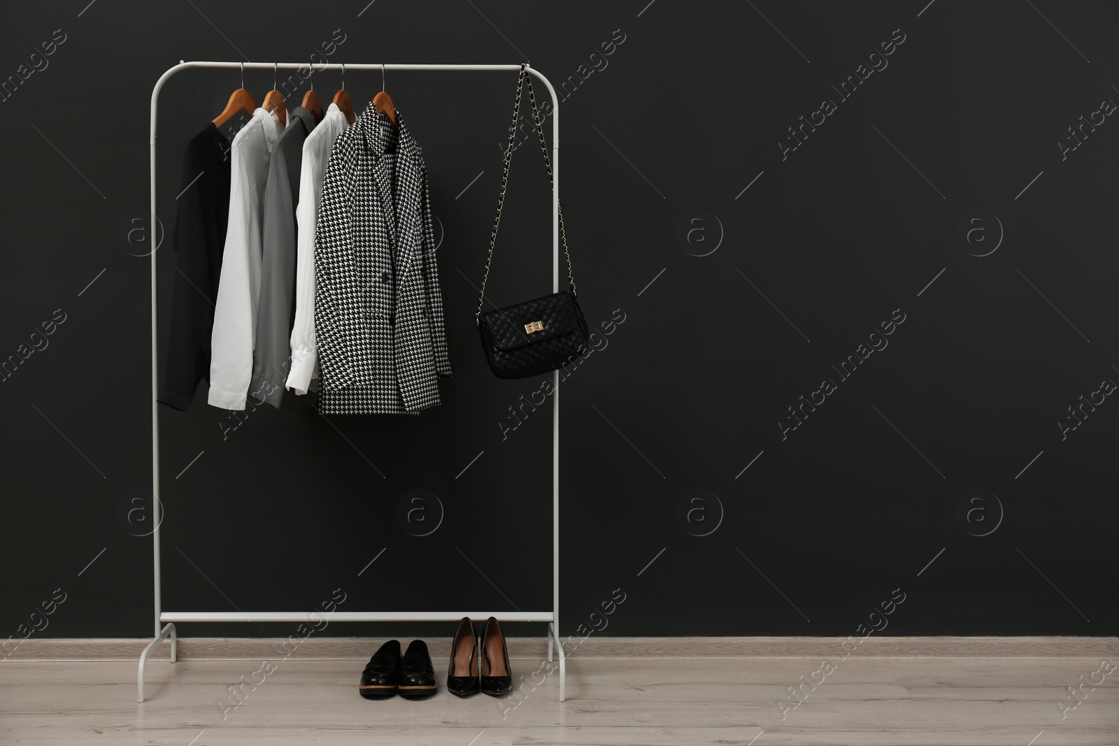 Photo of Rack with stylish clothes near black wall. Space for text