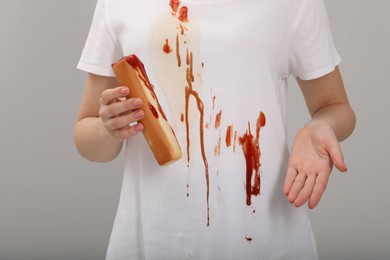 Photo of Woman holding hotdog and showing stain from sauce on her shirt against light grey background, closeup