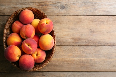 Photo of Fresh sweet peaches in wicker bowl on wooden table, top view