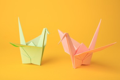 Origami art. Beautiful light green and pale pink paper cranes on orange background