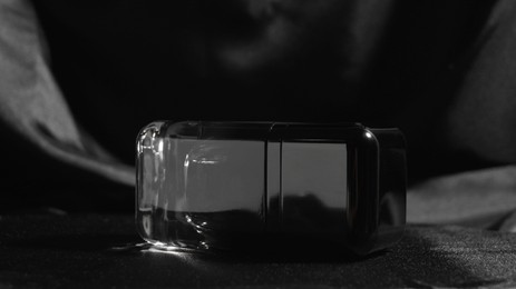 Photo of Luxury bottle of perfume on black silk, closeup