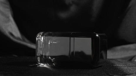 Luxury bottle of perfume on black silk, closeup