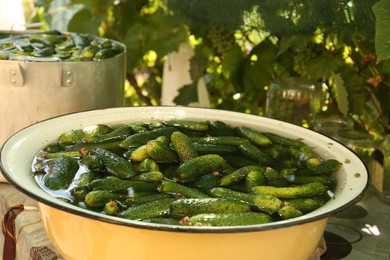 Photo of Fresh ripe cucumbers with water in metal bowl on table outdoors, closeup